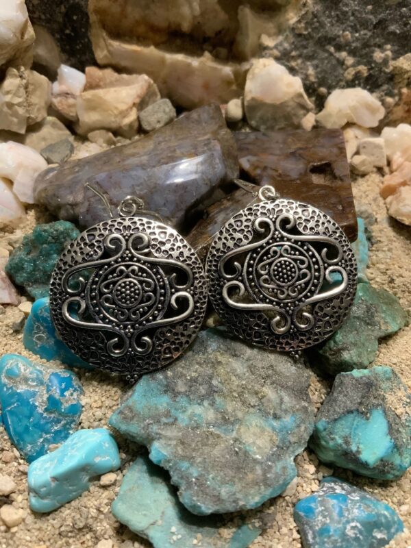 Intricate silver earrings displayed on rocks
